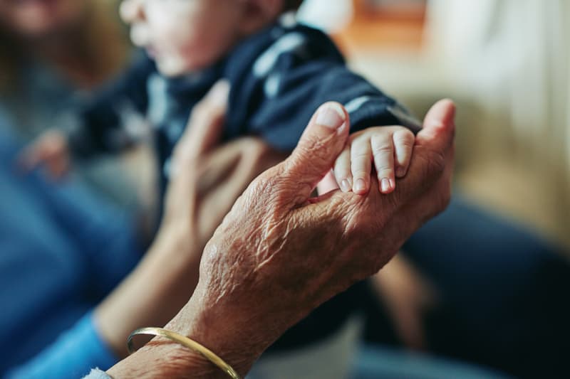 Ältere Hand hält behutsam die kleine Hand eines Babys